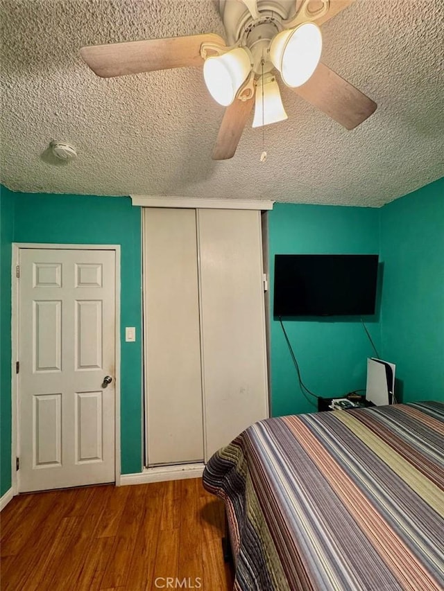 bedroom with a textured ceiling, wood finished floors, a closet, and a ceiling fan