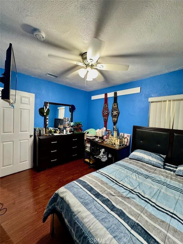 bedroom with a textured ceiling, wood finished floors, ceiling fan, and visible vents