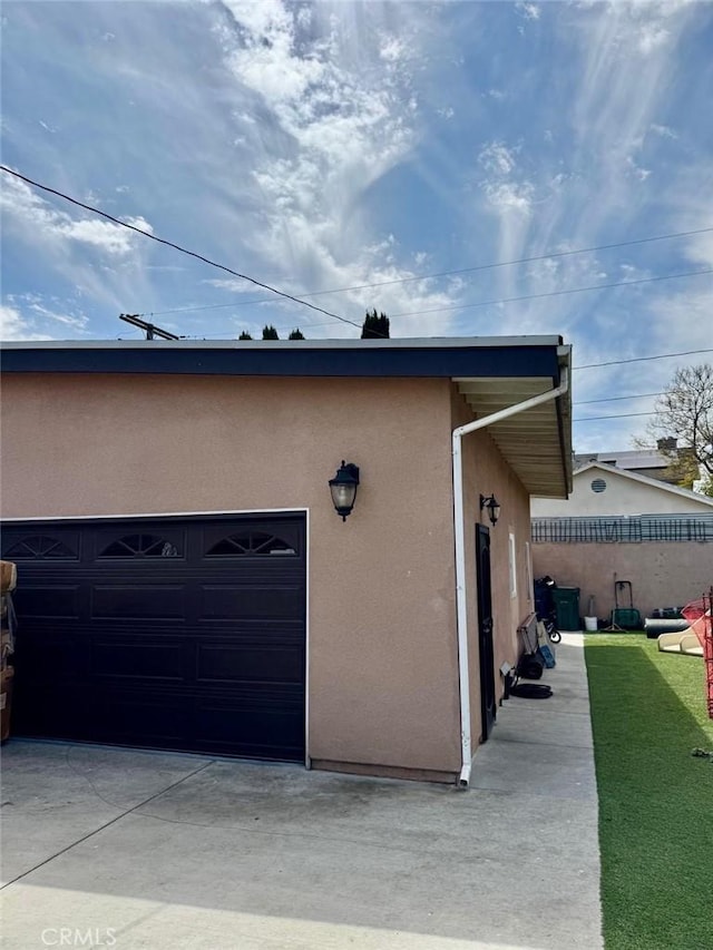 view of side of property featuring fence, a garage, driveway, and stucco siding