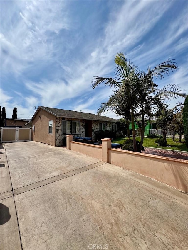 single story home featuring driveway, a fenced front yard, stucco siding, and stone siding