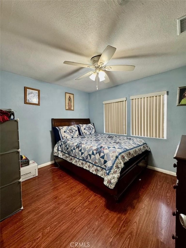 bedroom with visible vents, baseboards, a textured ceiling, and wood finished floors