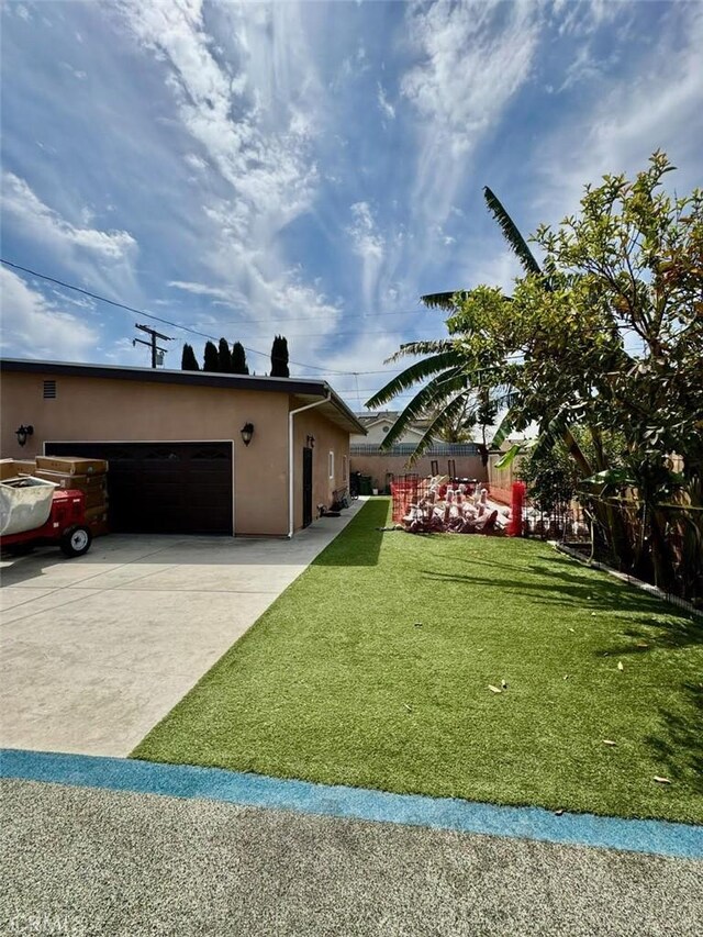 exterior space featuring stucco siding, driveway, a garage, fence, and a lawn