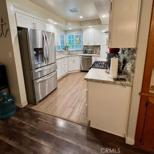 11406 Christy Ave, Sylmar, CA 91342 - kitchen with stainless steel appliances, a sink, backsplash, white cabinetry, and wood finished floors