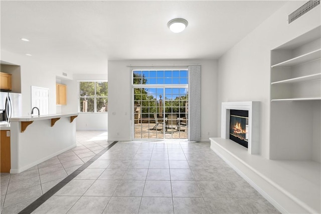 unfurnished living room featuring a sink, light tile patterned flooring, a glass covered fireplace, visible vents, and baseboards