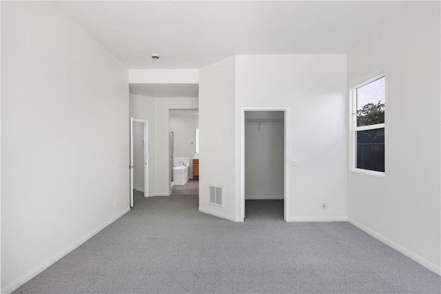 unfurnished bedroom with a walk in closet, visible vents, carpet, and baseboards