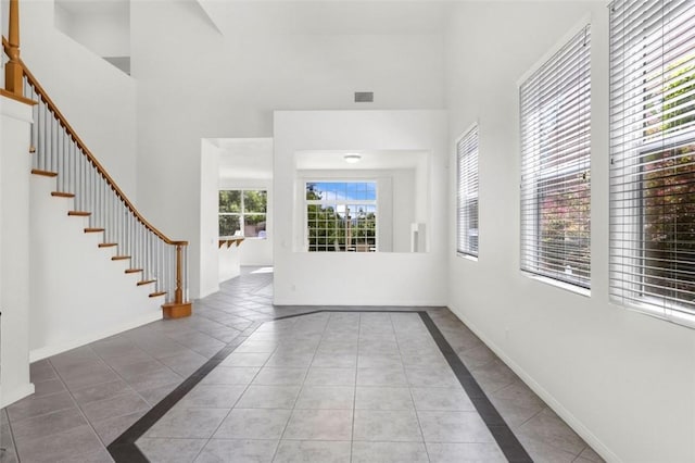 foyer entrance featuring visible vents, baseboards, a high ceiling, tile patterned flooring, and stairs