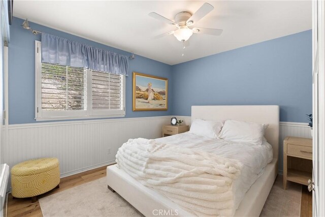 bedroom featuring a wainscoted wall, wood finished floors, and a ceiling fan
