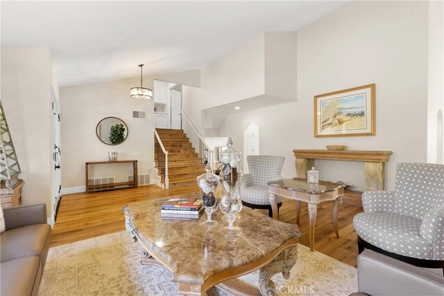 living room featuring wood finished floors, stairs, arched walkways, baseboards, and lofted ceiling