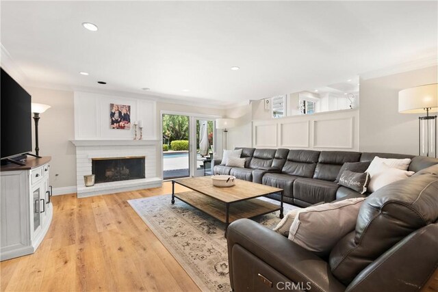 living room featuring a brick fireplace, recessed lighting, light wood-style floors, and crown molding