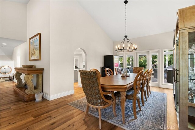 dining area featuring arched walkways, baseboards, a chandelier, light wood-style flooring, and high vaulted ceiling