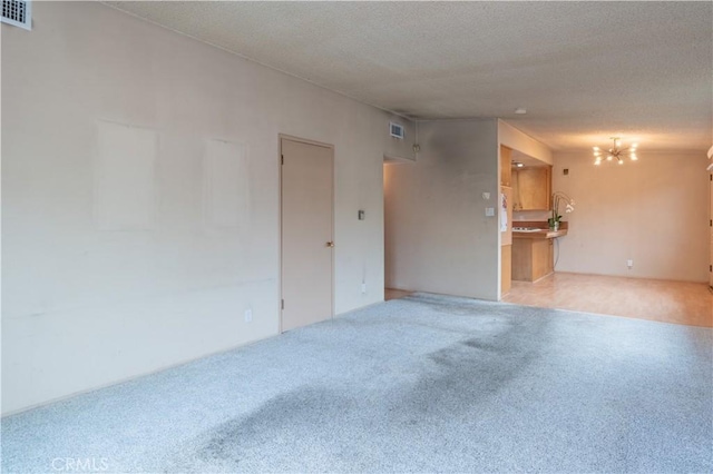 empty room with visible vents, carpet, a textured ceiling, and a chandelier