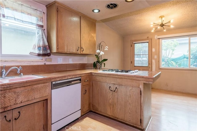 kitchen featuring a sink, a peninsula, tile countertops, and white appliances