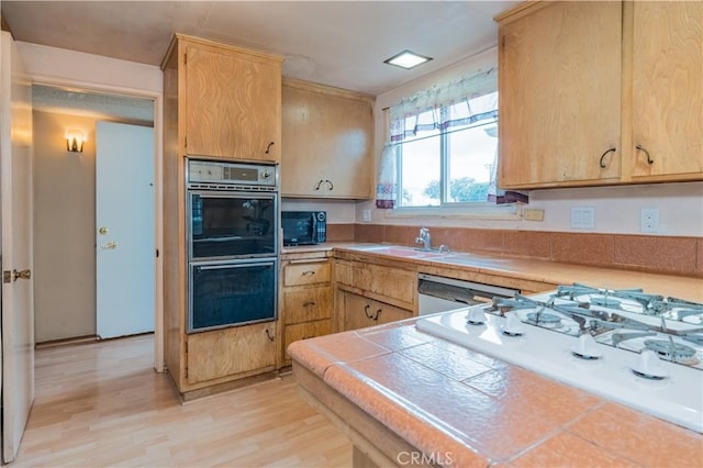 kitchen with black microwave, double oven, light wood-style floors, white gas cooktop, and tile countertops