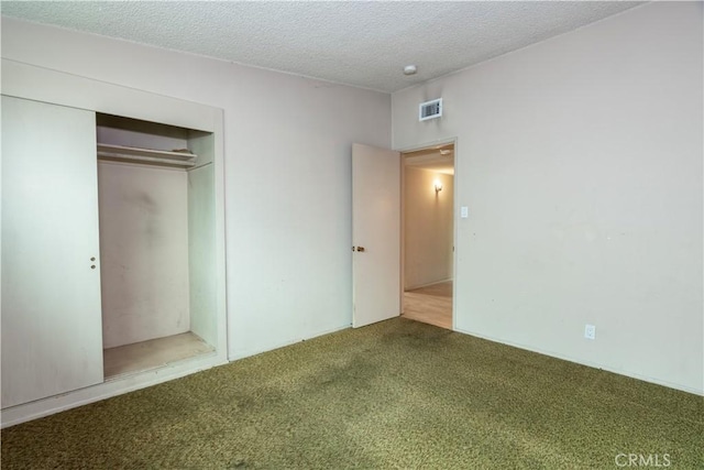 unfurnished bedroom with a textured ceiling, visible vents, carpet, and a closet