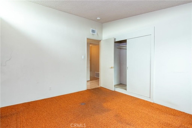 unfurnished bedroom with a closet, carpet flooring, a textured ceiling, and visible vents