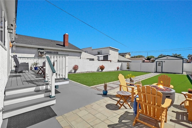 view of patio / terrace with a fenced backyard, an outdoor structure, an outdoor fire pit, a storage unit, and a deck