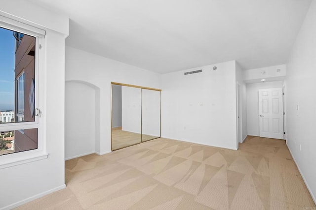 unfurnished bedroom featuring light colored carpet, a closet, visible vents, and baseboards