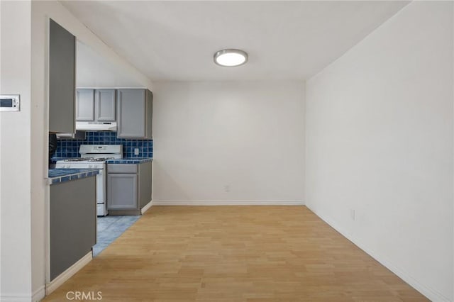 5055 Coldwater Canyon Ave Unit 105, Sherman Oaks, CA 91423 - kitchen with white range with gas stovetop, gray cabinetry, under cabinet range hood, decorative backsplash, and light wood finished floors