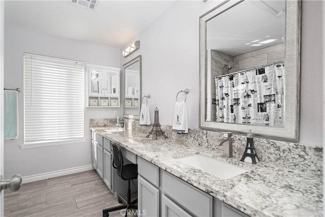 bathroom featuring a tile shower, visible vents, a sink, double vanity, and baseboards