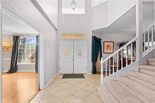 foyer featuring stairs, light tile patterned floors, a high ceiling, and baseboards