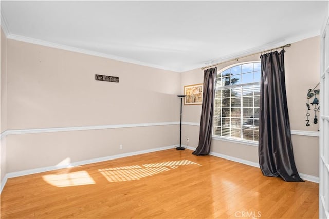 spare room featuring light wood-style flooring, crown molding, and baseboards