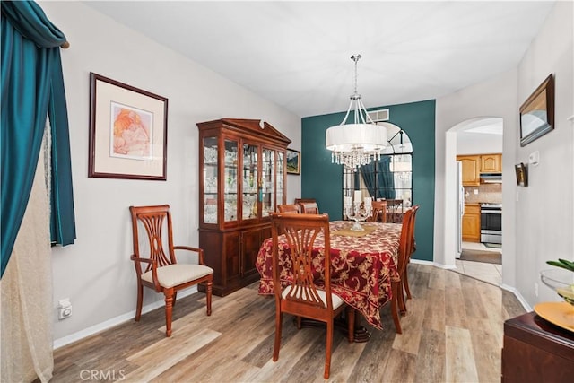 dining space with arched walkways, light wood finished floors, a notable chandelier, and baseboards