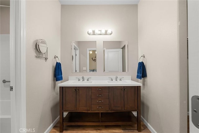 full bath featuring double vanity, baseboards, a sink, and wood finished floors