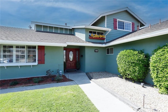 property entrance featuring roof with shingles, stucco siding, and a lawn