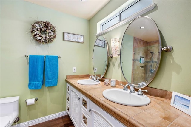 bathroom featuring toilet, tiled shower, double vanity, and a sink