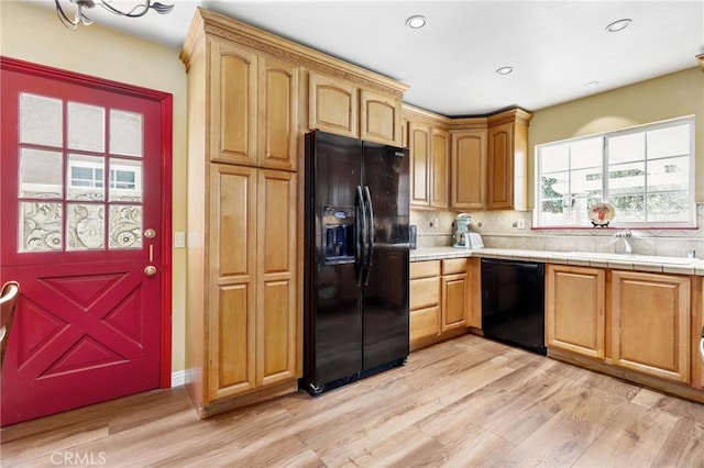 kitchen with light wood-type flooring, a sink, backsplash, and black appliances