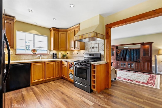 kitchen with custom exhaust hood, black appliances, light wood-style floors, and a sink