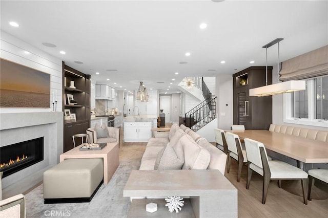 living area with a glass covered fireplace, recessed lighting, stairway, and light wood-style flooring