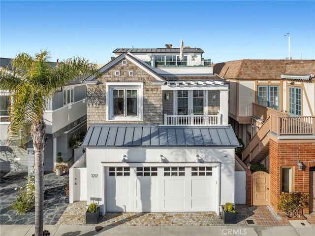 view of front of property with a standing seam roof, metal roof, a balcony, an attached garage, and driveway