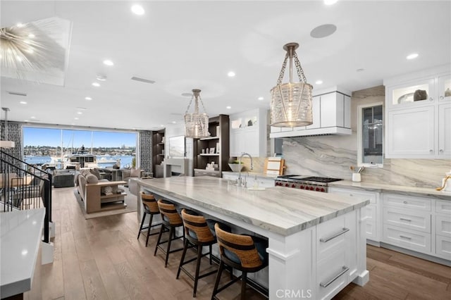 kitchen with a sink, white cabinetry, a spacious island, backsplash, and range