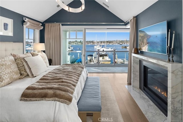 bedroom with a high end fireplace, multiple windows, wood finished floors, and lofted ceiling