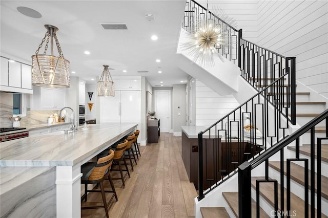 interior space with a large island, white cabinetry, light wood-style floors, visible vents, and a sink