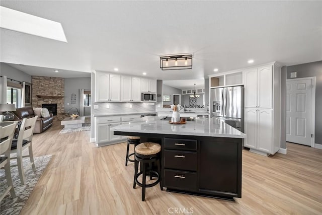 kitchen with a breakfast bar, open floor plan, white cabinets, light wood-style floors, and stainless steel appliances