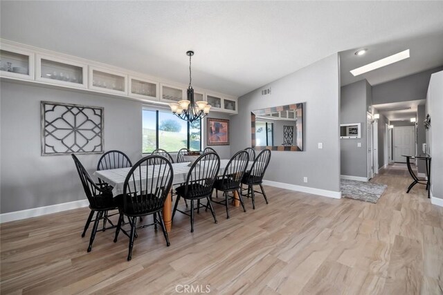 dining area featuring baseboards, a chandelier, visible vents, lofted ceiling, and light wood finished floors