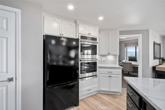 kitchen featuring freestanding refrigerator, light stone countertops, white cabinets, light wood finished floors, and stainless steel double oven