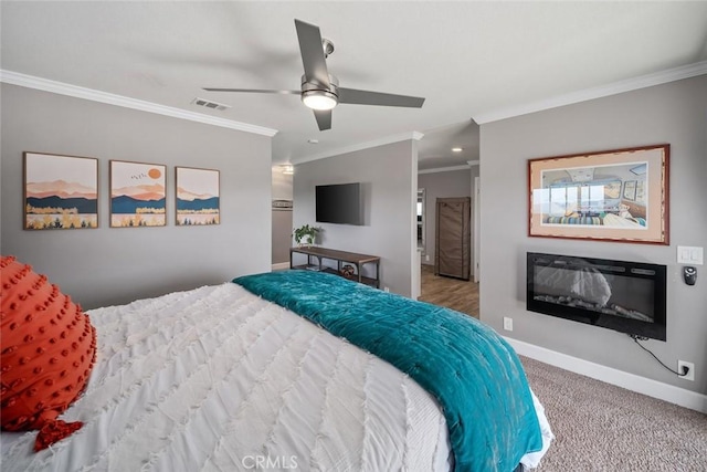 bedroom featuring crown molding, a glass covered fireplace, visible vents, carpet flooring, and baseboards