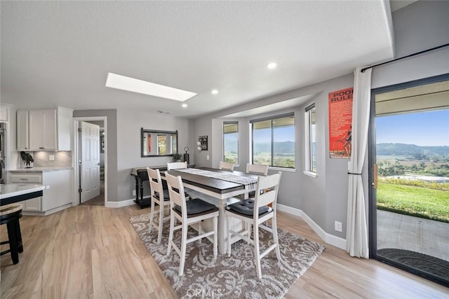 dining space with light wood-style floors, baseboards, a textured ceiling, and a skylight