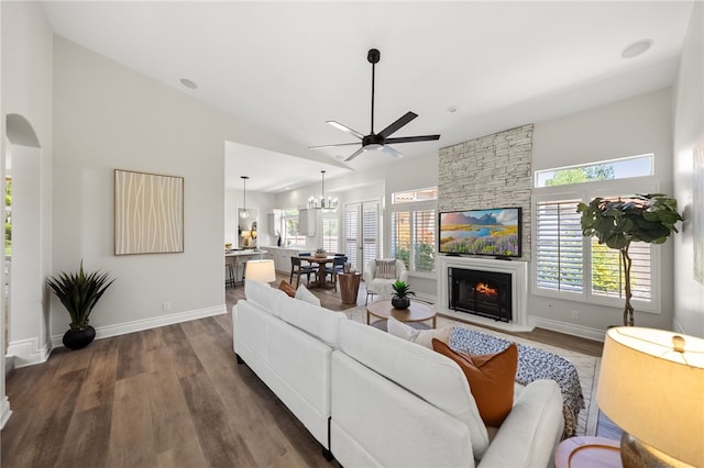 living room with wood finished floors, a stone fireplace, baseboards, high vaulted ceiling, and ceiling fan with notable chandelier
