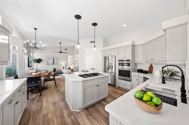 38027 Cherrywood Dr, Murrieta, CA 92562 - kitchen featuring appliances with stainless steel finishes, backsplash, light wood-type flooring, a center island, and light countertops