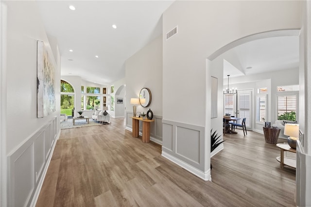 corridor featuring a decorative wall, wood finished floors, arched walkways, a wainscoted wall, and lofted ceiling
