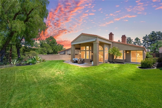 back of property at dusk featuring a lawn, a patio, a chimney, and stucco siding