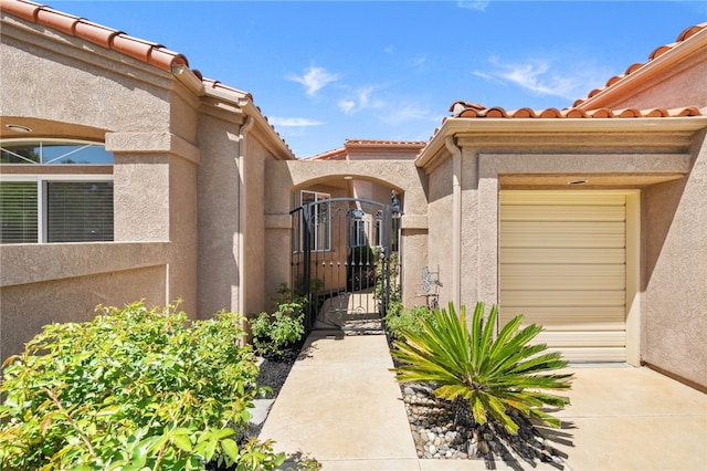 entrance to property with a gate, a tiled roof, and stucco siding