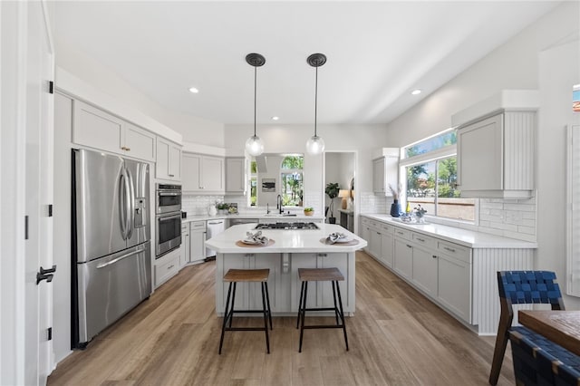 kitchen featuring backsplash, light countertops, light wood-type flooring, appliances with stainless steel finishes, and a breakfast bar area