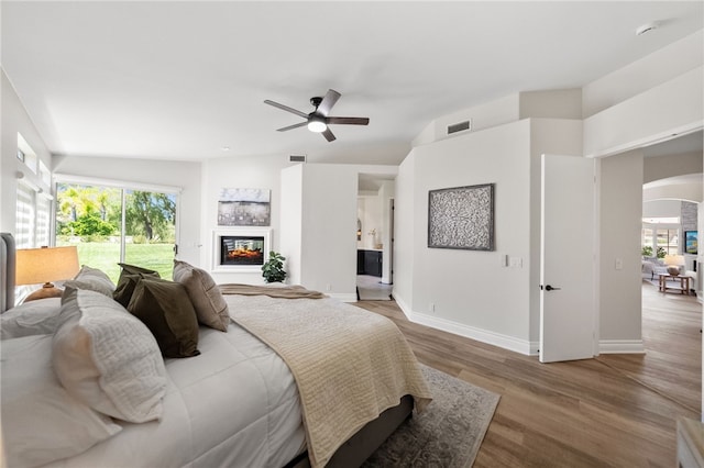 bedroom featuring wood finished floors, a glass covered fireplace, arched walkways, baseboards, and visible vents