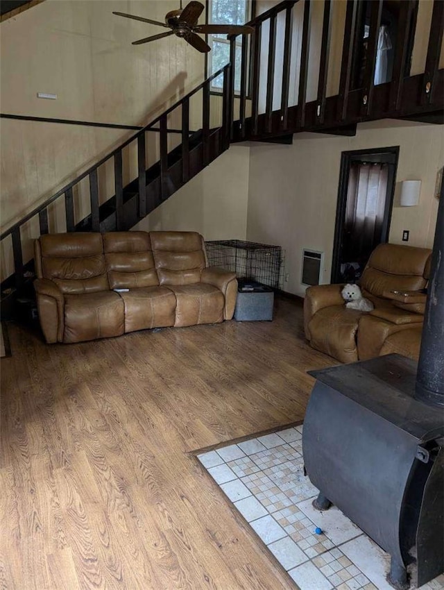living room with heating unit, wood finished floors, stairs, ceiling fan, and a towering ceiling