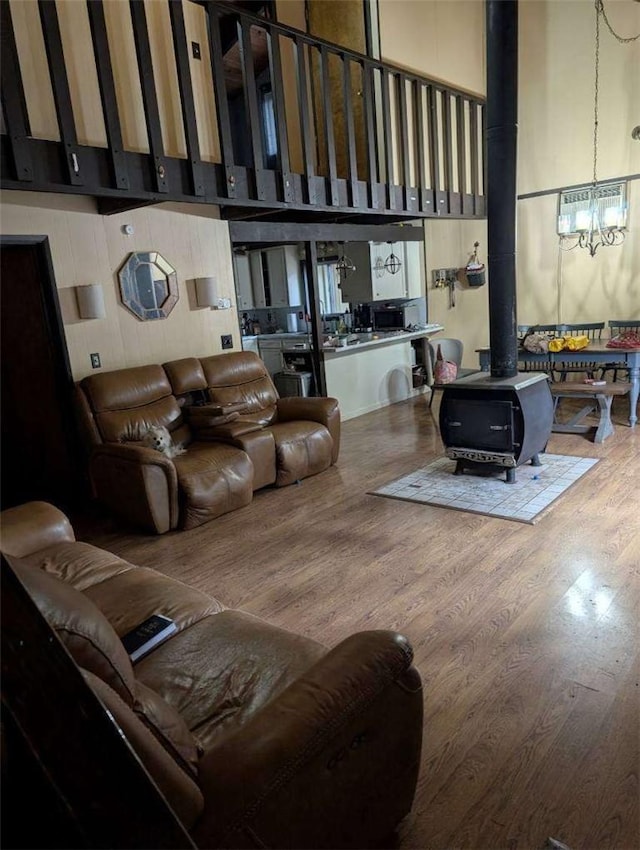 living room featuring wood finished floors, a wood stove, a towering ceiling, and an inviting chandelier